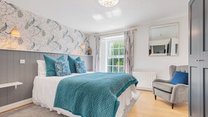 Ein Schlafzimmer mit einem Bett, einem grauen Sessel, einem Heizkörper und einem Fenster mit Vorhängen.