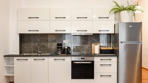 Una cocina moderna con gabinetes blancos, un refrigerador de acero inoxidable, un horno empotrado y una cafetera.