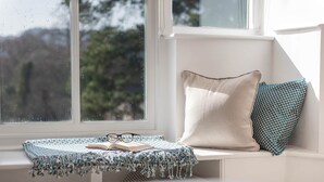Ein Fensterplatz mit Kissen, einer gemusterten Decke und einem Buch.