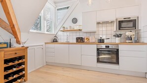 Eine moderne Küche mit weißen Schränken, einem Einbauofen und einem Fenster mit Jalousien.