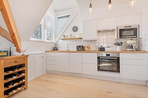 A modern kitchen with white cabinetry, a built-in oven, and a window with blinds. - Grandsire, Luxury 3 bedroom apartment (Windermere) (Windermere)