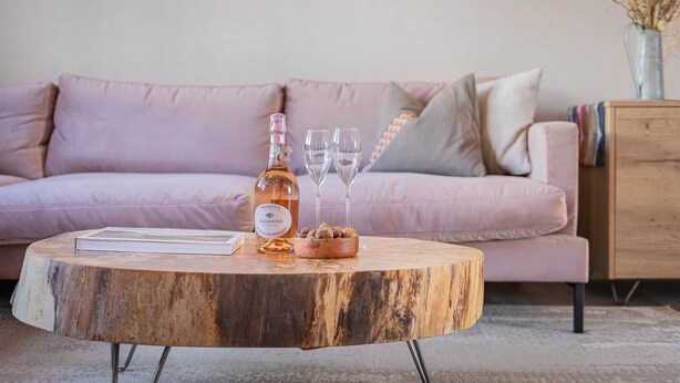 A round wooden coffee table with a bottle of Prosecco and two glasses on it, placed in front of a pink sofa. - Esperance - Brand New Luxury studio with parking! (Windermere)