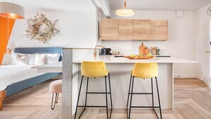 A modern kitchen with wooden cabinets, a white countertop, and two yellow bar stools. - Esperance - Brand New Luxury studio with parking! (Windermere)
