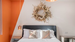 A bedroom with a bed, a nightstand, a bedside table, a wall-mounted light, and a decorative wreath. - Esperance - Brand New Luxury studio with parking! (Windermere)