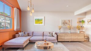 A modern living room with a sectional sofa, a wooden coffee table, and a view of the outdoors through large windows. - Esperance - Brand New Luxury studio with parking! (Windermere)