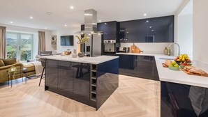 Une cuisine moderne dotée d’un îlot central, de meubles de rangement aux couleurs sombres et offrant une vue sur l’extérieur.