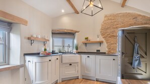 A kitchen with white cabinets, a wooden countertop, a stone accent wall, and a hanging light fixture. - The Hut Retreat - Kirkby Lonsdale (Kirkby Lonsdale)