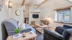 A cozy living room with a stone fireplace, a television, and a comfortable seating area with a sofa and armchairs. - The Hut Retreat - Kirkby Lonsdale (Kirkby Lonsdale)