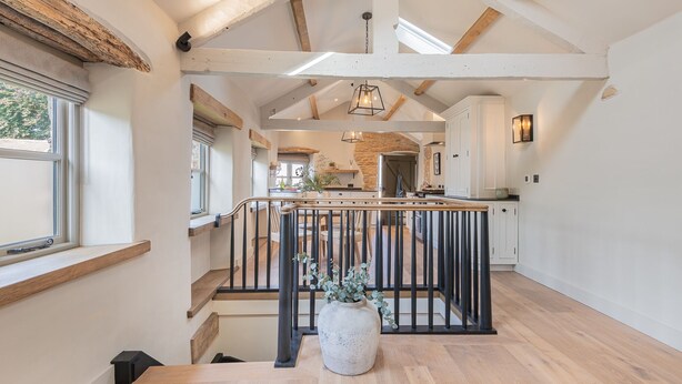 A spacious interior with a high ceiling, exposed wooden beams, a central staircase, and a kitchen area with stone accents. - The Hut Retreat - Kirkby Lonsdale (Kirkby Lonsdale)