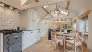A kitchen with white cabinets, a stove, and a dining area with wooden chairs and a table. - The Hut Retreat - Kirkby Lonsdale (Kirkby Lonsdale)