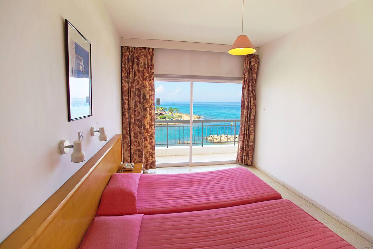 Habitación de hotel con una cama grande, vistas al mar y un balcón con barandilla.