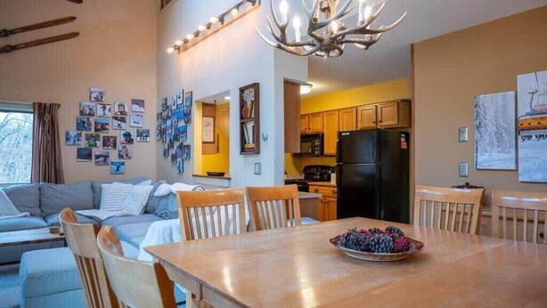 A modern living room with a dining table, wooden chairs, a sofa, and a chandelier. - Cozy Kettlebrook 2BR: Ski Access, Fireplace & Deck (Ludlow)
