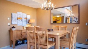A dining area with a wooden table and chairs, a chandelier, a large mirror, and artwork on the wall. - Cozy Kettlebrook 2BR: Ski Access, Fireplace & Deck (Ludlow)
