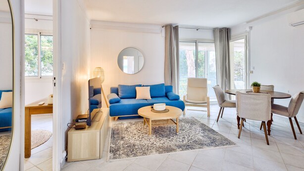 Een moderne woonkamer met een blauwe bank, een ronde salontafel en een eethoek met een tafel en stoelen.