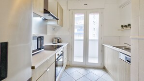 Een kleine keuken met witte keukenkastjes, een inbouwoven, een magnetron en een spoelbak.