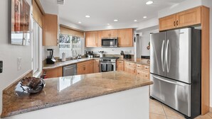 A modern kitchen with granite countertops, stainless steel appliances, wooden cabinets, and a large island. - Pacific Beach Gem: Rooftop Deck, Bay Views, AC & Pet Friendly (San Diego)