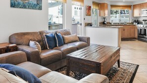 A modern living room with a leather sofa, wooden coffee table, and a kitchen in the background. - Pacific Beach Gem: Rooftop Deck, Bay Views, AC & Pet Friendly (San Diego)