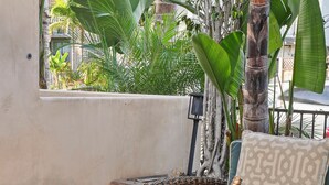 A wicker sofa with cushions, a small table with a bottle and glasses, and a bowl of salad. - Pacific Beach Gem: Rooftop Deck, Bay Views, AC & Pet Friendly (San Diego)