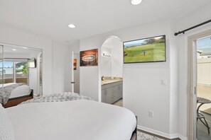 A bedroom with a large bed, a bathroom with a sink and cabinets, and a TV displaying a golf course. - Sail Bay Dream | Rooftop Patio, Bay Views, AC, Garage, Pinball, Paddle Boards + Bikes (San Diego)