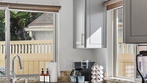 A modern kitchen with a granite countertop, stainless steel appliances, and a window with a view of a wooden fence and greenery. - Sail Bay Dream | Rooftop Patio, Bay Views, AC, Garage, Pinball, Paddle Boards + Bikes (San Diego)