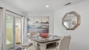 A dining area with a table set for four, a large painting, and a decorative mirror. - Sail Bay Dream | Rooftop Patio, Bay Views, AC, Garage, Pinball, Paddle Boards + Bikes (San Diego)