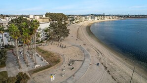A beach with a curved walkway, palm trees, and a view of the ocean. - Sail Bay Dream | Rooftop Patio, Bay Views, AC, Garage, Pinball, Paddle Boards + Bikes (San Diego)