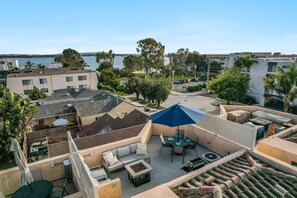 A rooftop patio with outdoor furniture, a blue umbrella, and a view of the sea. - Sail Bay Dream | Rooftop Patio, Bay Views, AC, Garage, Pinball, Paddle Boards + Bikes (San Diego)