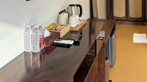 A hotel room with a wooden reception desk, a flat-screen TV mounted on the wall, a coffee maker, and a tray with cups and a kettle. - Kashi Anandam Spiritual & Wellness Vedic Village (Varanasi)