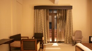 A hotel room with a bed, two chairs, a small table, and a window with curtains. - Kashi Anandam Spiritual & Wellness Vedic Village (Varanasi)