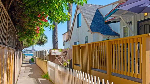 A narrow sidewalk flanked by wooden fences and houses with balconies. - Bay View Cottage | Patio, W/D, Parking, Location! (San Diego)