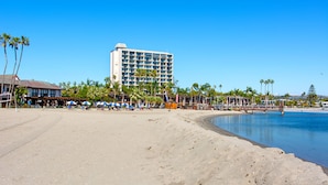 A beach with a hotel in the background, palm trees, and a clear sky. - Bay View Cottage | Patio, W/D, Parking, Location! (San Diego)