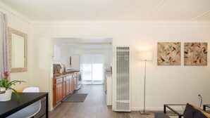 A modern living room with a sofa, a dining table with chairs, a kitchen in the background, and a floor lamp. - Bay View Cottage | Patio, W/D, Parking, Location! (San Diego)