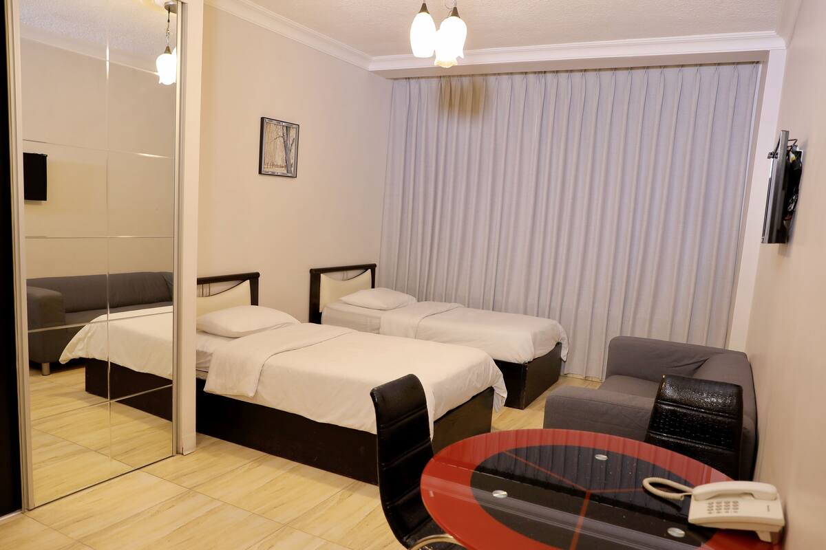 A hotel room with two beds, a sofa, a glass table with a phone, and a mirror.