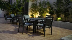 Zona patio esterna con tavolo e sedie, circondata da piante e un muro.