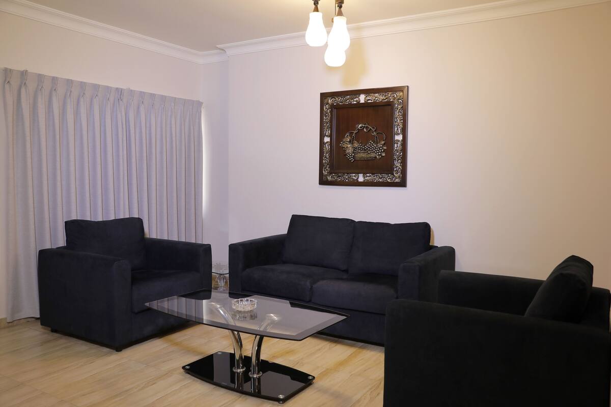 A living room with a dark blue sofa set, a glass coffee table, and a framed picture on the wall.