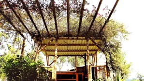 A covered outdoor area with a wooden structure, surrounded by greenery and trees. - Casa Laureles (Filandia)