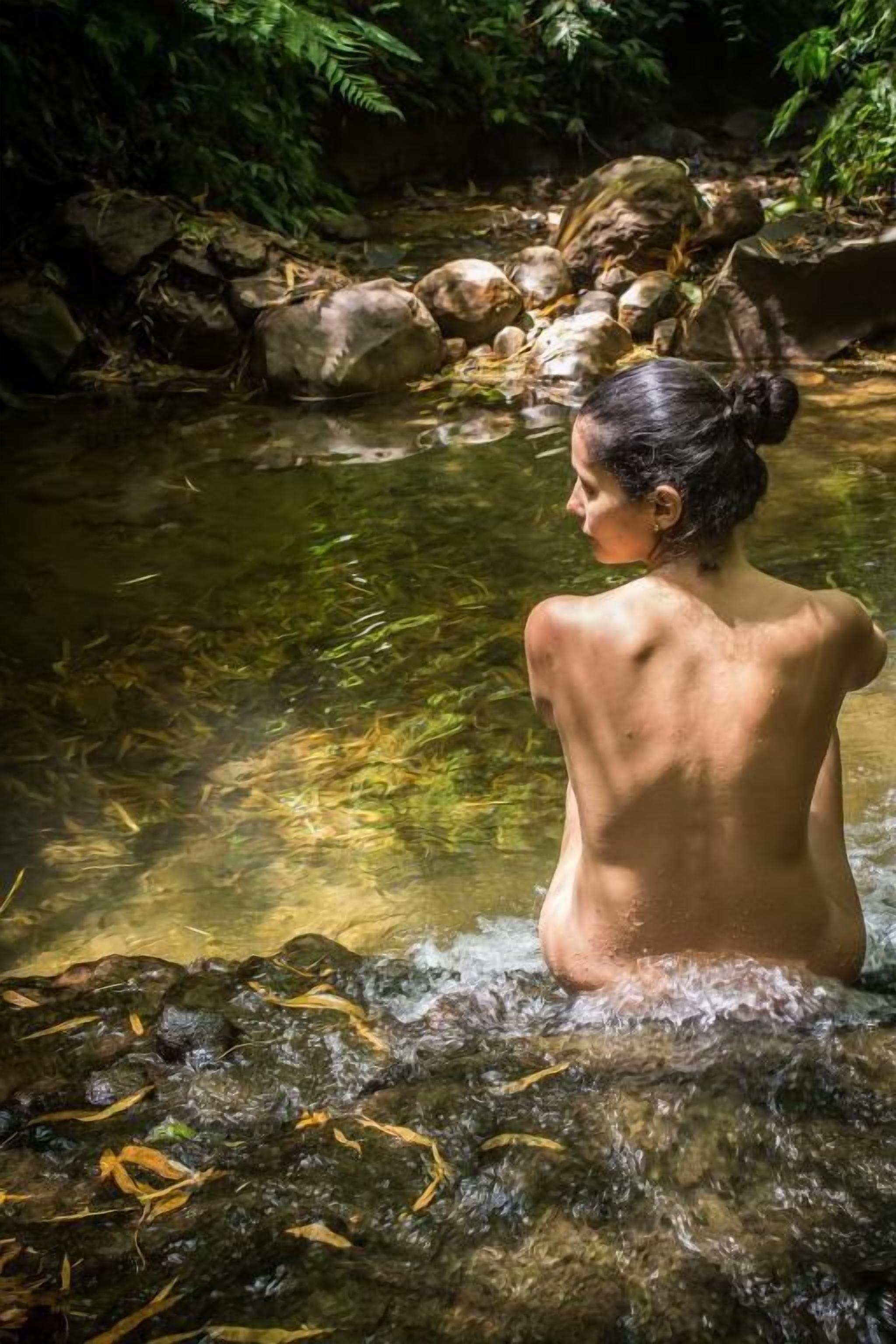 A person standing in a natural water setting surrounded by rocks and greenery.