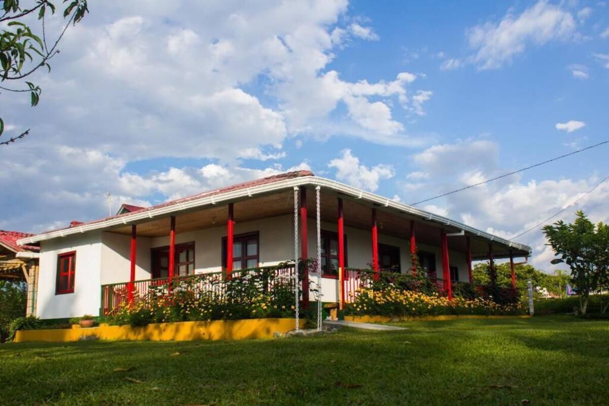 A two-story house with a red and white exterior, a covered porch with red pillars, and a well-maintained garden.