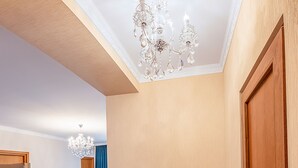 Een ruime woonkamer met houten vloeren, een kroonluchter, een houten deur en een zithoek met fauteuils en een televisie.