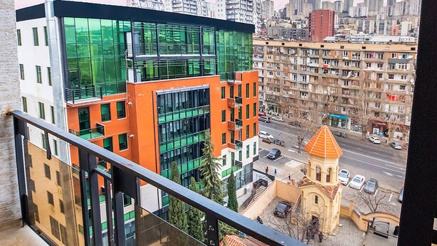 Een balkon met uitzicht op moderne gebouwen en een traditionele kerk.