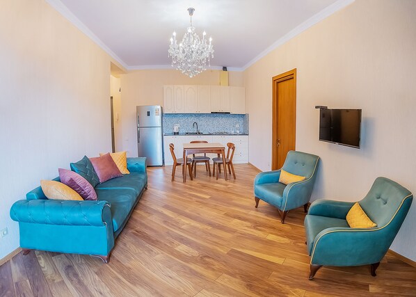 A living room with a sofa, two armchairs, a dining table with chairs, a kitchen area, and a TV mounted on the wall. - HB apartments Vazha Pshavela (Tbilisi)