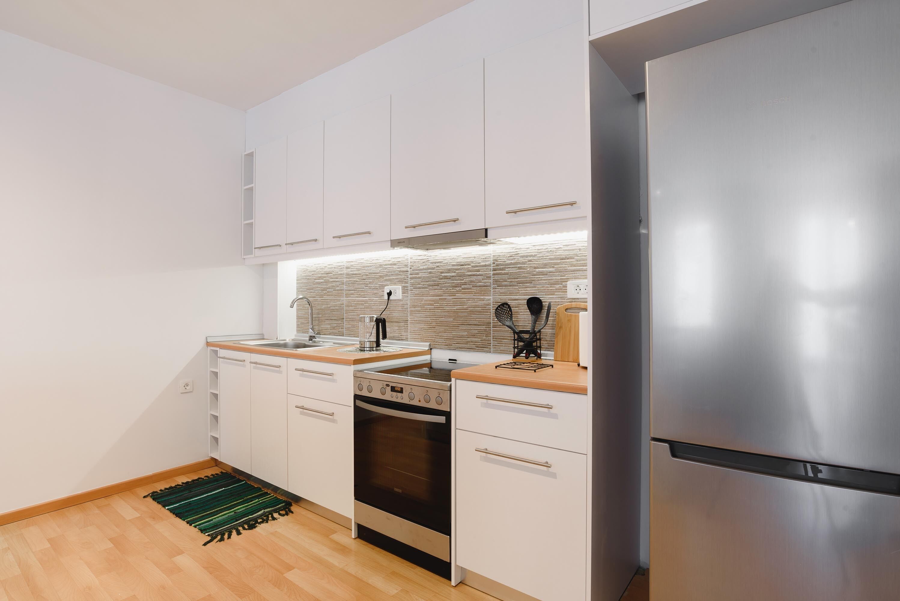 A modern kitchen with white cabinets, stainless steel appliances, a wooden countertop, and a green rug.