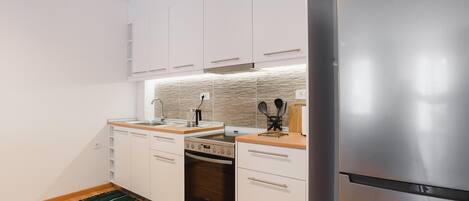A modern kitchen with white cabinets, stainless steel appliances, a wooden countertop, and a green rug.