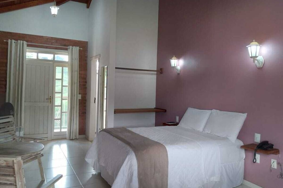 Quarto com cama, mesa de cabeceira, abajur e vista para o exterior.
