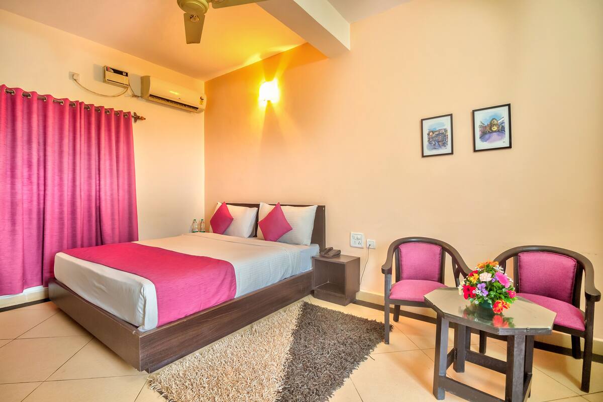 A bedroom with a bed, nightstand, chairs, and a small table with flowers.