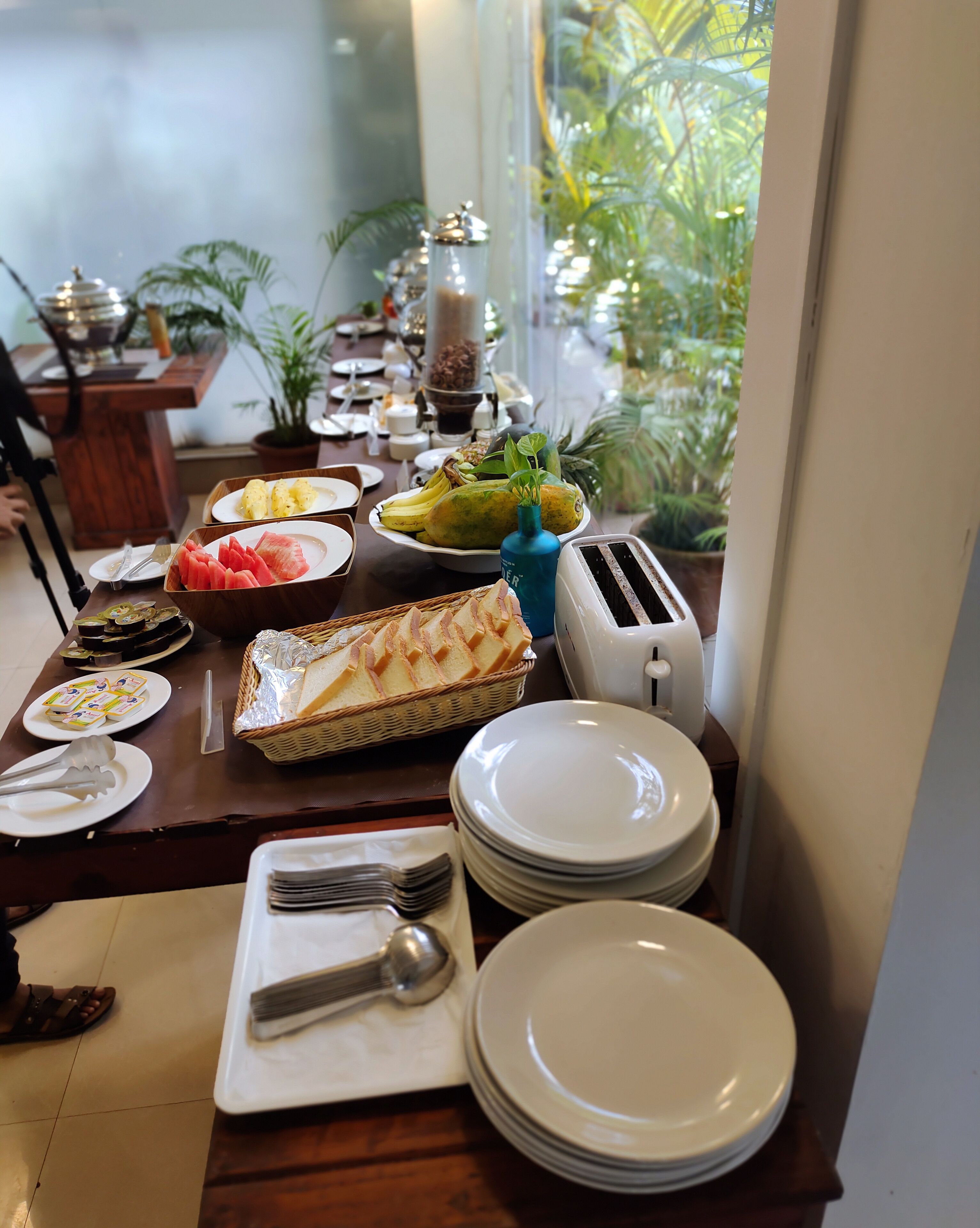 A breakfast buffet with various food items, plates, and utensils on a wooden table.
