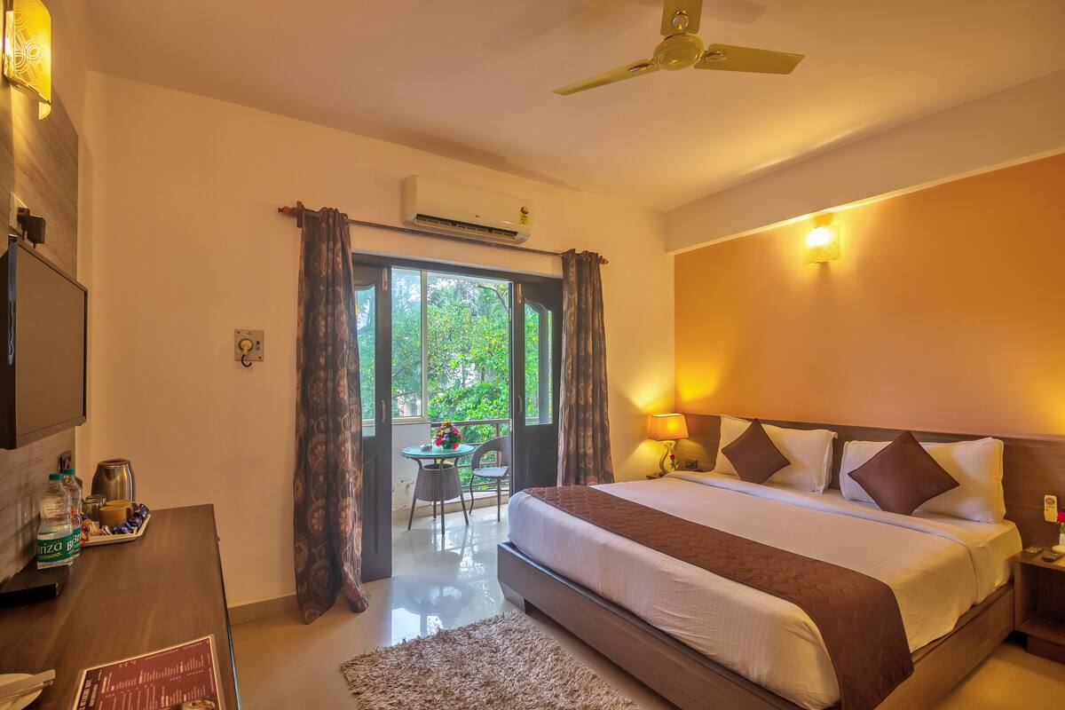 A hotel room with a large bed, bedside lamps, a television, and a balcony with a table and chairs.