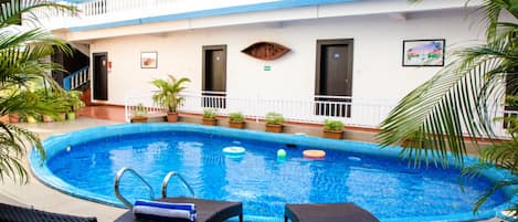 A swimming pool with lounge chairs, potted plants, and a building with balconies and windows.