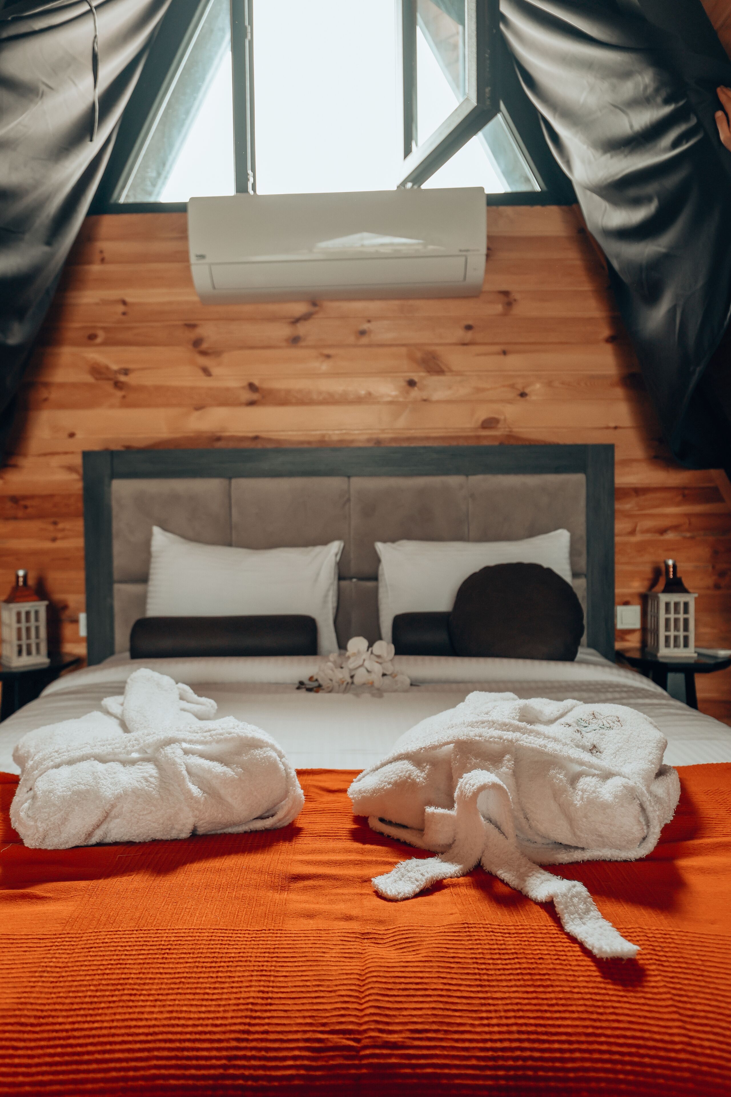 A cozy room with a wooden ceiling, a large bed with two pillows, and a window with curtains.