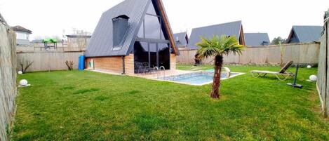 Une maison moderne dotée d’un toit triangulaire original, d’une piscine et d’un petit palmier.